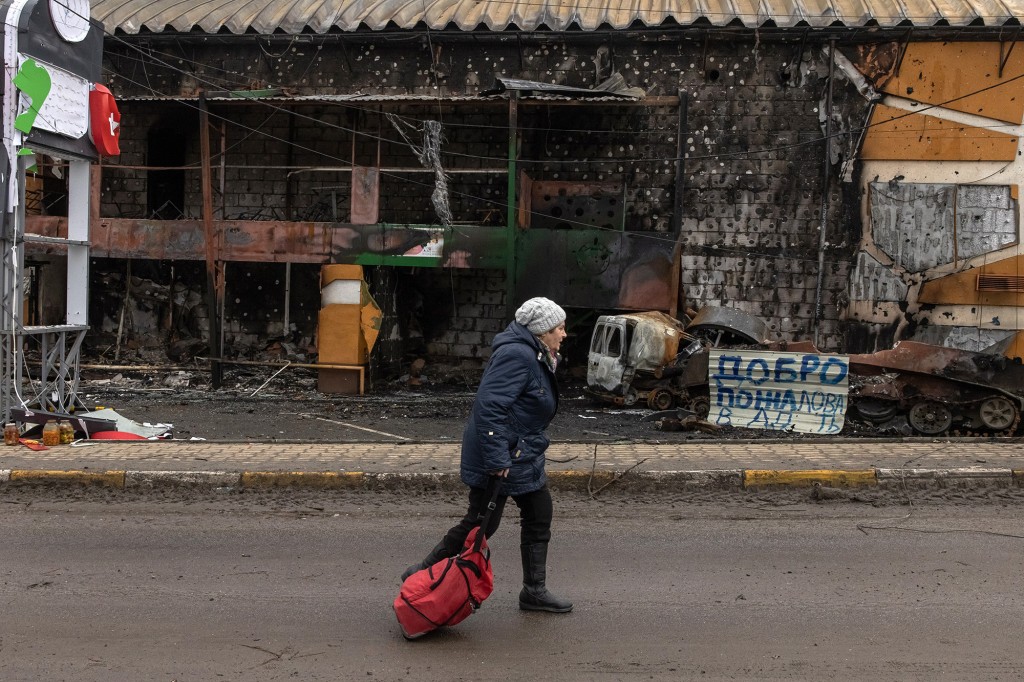 Eine Frau, die einen Koffer aus der Stadt Bucha trägt, geht an einem zerstörten Gebäude an der Frontlinie in der Stadt Irbin, Region Kiew (Kiew), Ukraine, am 04